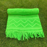 Green towel with zigzag pattern and fringes on grass