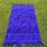 Blue towel with geometric patterns and fringes on a grassy background