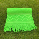 Green towel with zigzag pattern and fringes on grass