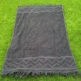 Dark gray towel with fringes on a grassy background