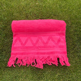 Pink towel with geometric pattern and fringes on grass