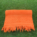 Orange towel with geometric pattern and fringes on grass