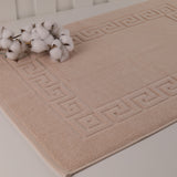 Beige bath mat with geometric pattern on a white surface, accompanied by cotton flowers.