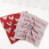 Two towels, one red with chicken patterns and one gray with French text, on a white background.