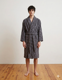 Man wearing a gray robe standing on a wooden floor with a white wall background