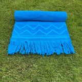 Blue towel with zigzag pattern and fringes on grass