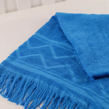 Turquoise beach towel with fringes on a white surface