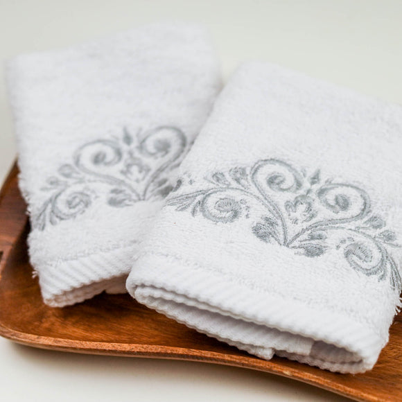 Two white towels with floral embroidery on a wooden tray