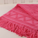 Pink textured blanket with fringes on a white surface
