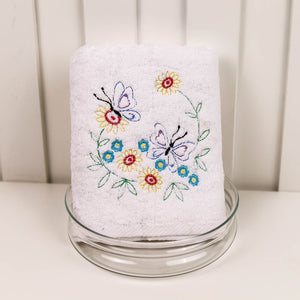 White towel with colorful butterfly and flower embroidery on a glass stand against a white background