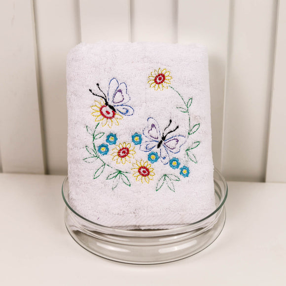 White towel with colorful butterfly and flower embroidery on a glass stand against a white background