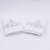 Two white towels with floral embroidery on a light gray background