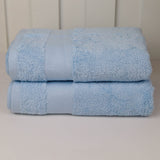 Two folded light blue cotton towels stacked on a light surface against a white paneled background.