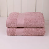 Two folded pink cotton towels stacked on a white surface against a white paneled background.