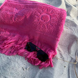 Pink towel with sunglasses on a sandy surface