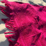 Close-up of a pink textured blanket with tassels on sandy ground