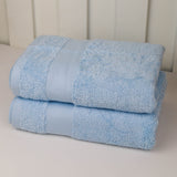 Two folded light blue cotton towels stacked on a white surface against a white paneled background.