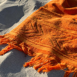 Orange towel with fringes on a sandy surface