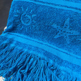 Blue towel with tassels and a logo on a textured surface