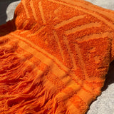 Orange textured beach towel with fringes on a sand surface