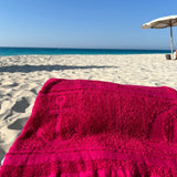 Fuchsia towel on a sandy beach with clear blue sky and ocean.
