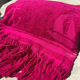 Close-up of a bright pink textured blanket with fringes on a light background
